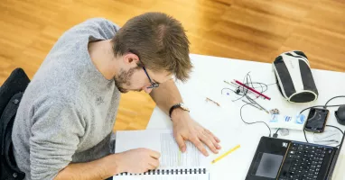Ragazzo che sta scrivendo con davanti portatile, astuccio e penne