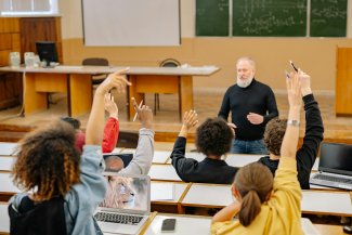 docente in aula e studenti con mani alzate