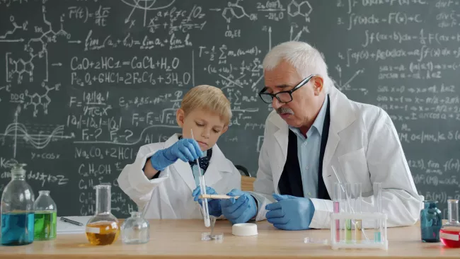 Anziano scienziato, probabilmente un professore o un ricercatore, che assiste un bambino durante un esperimento di chimica in un laboratorio