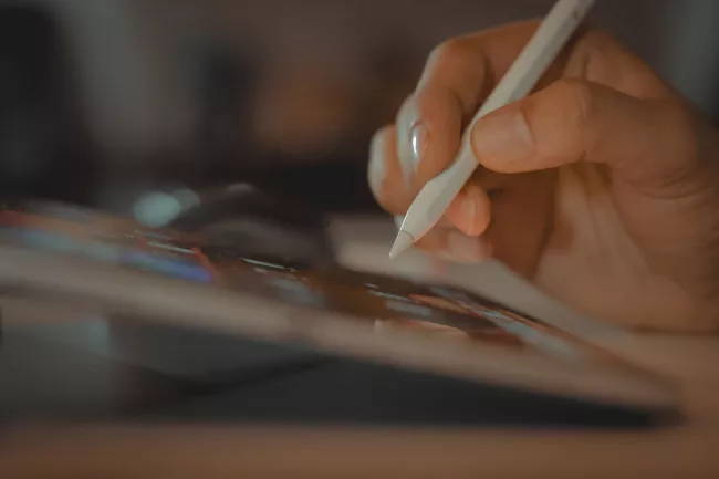 Dettaglio di una mano che impugna una penna digitale e la utilizza sulla superficie dello schermo di un tablet